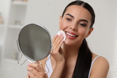 Photo of Beautiful woman removing makeup with cotton pad indoors