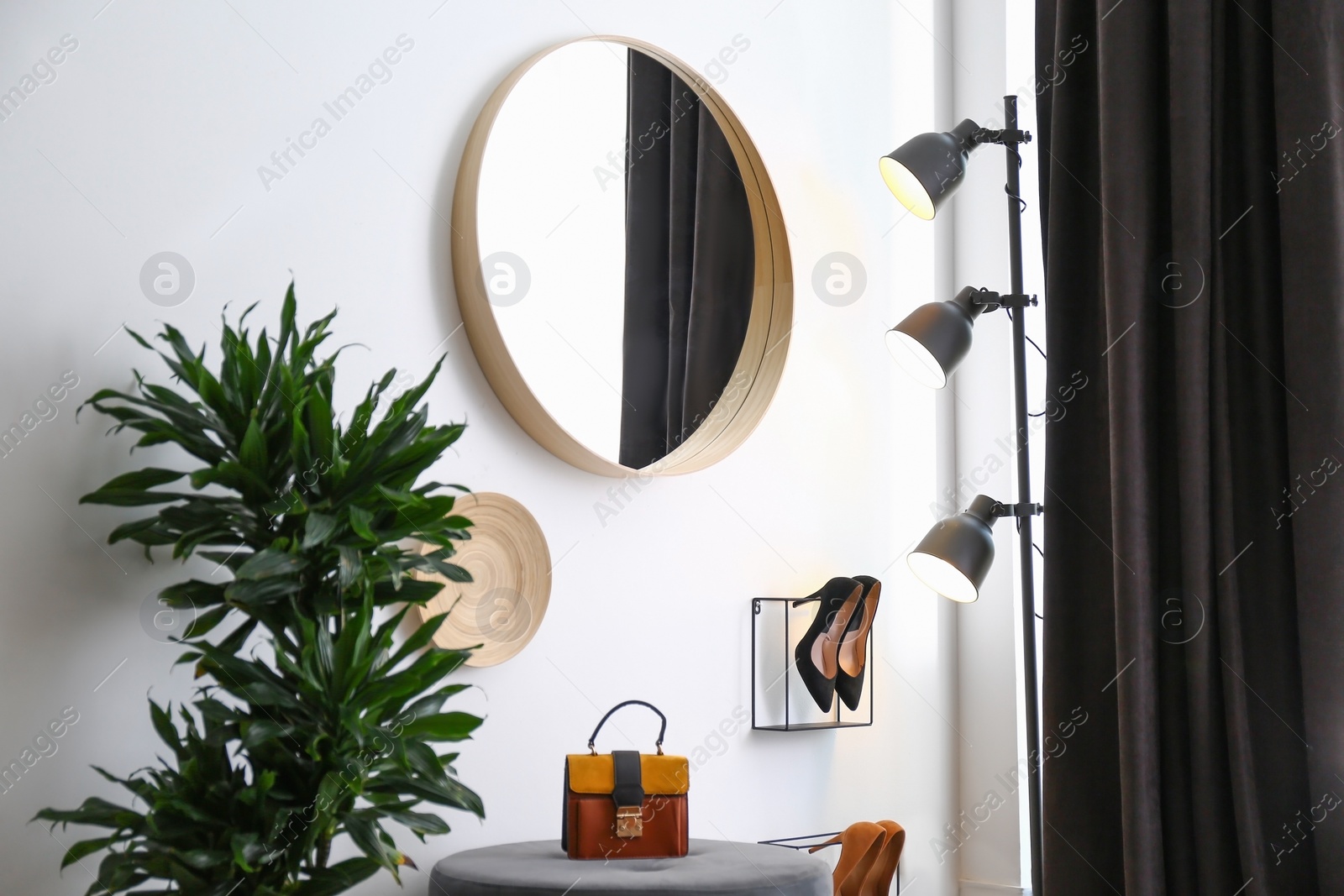 Photo of Big round mirror, houseplant and decor near white wall in hallway interior