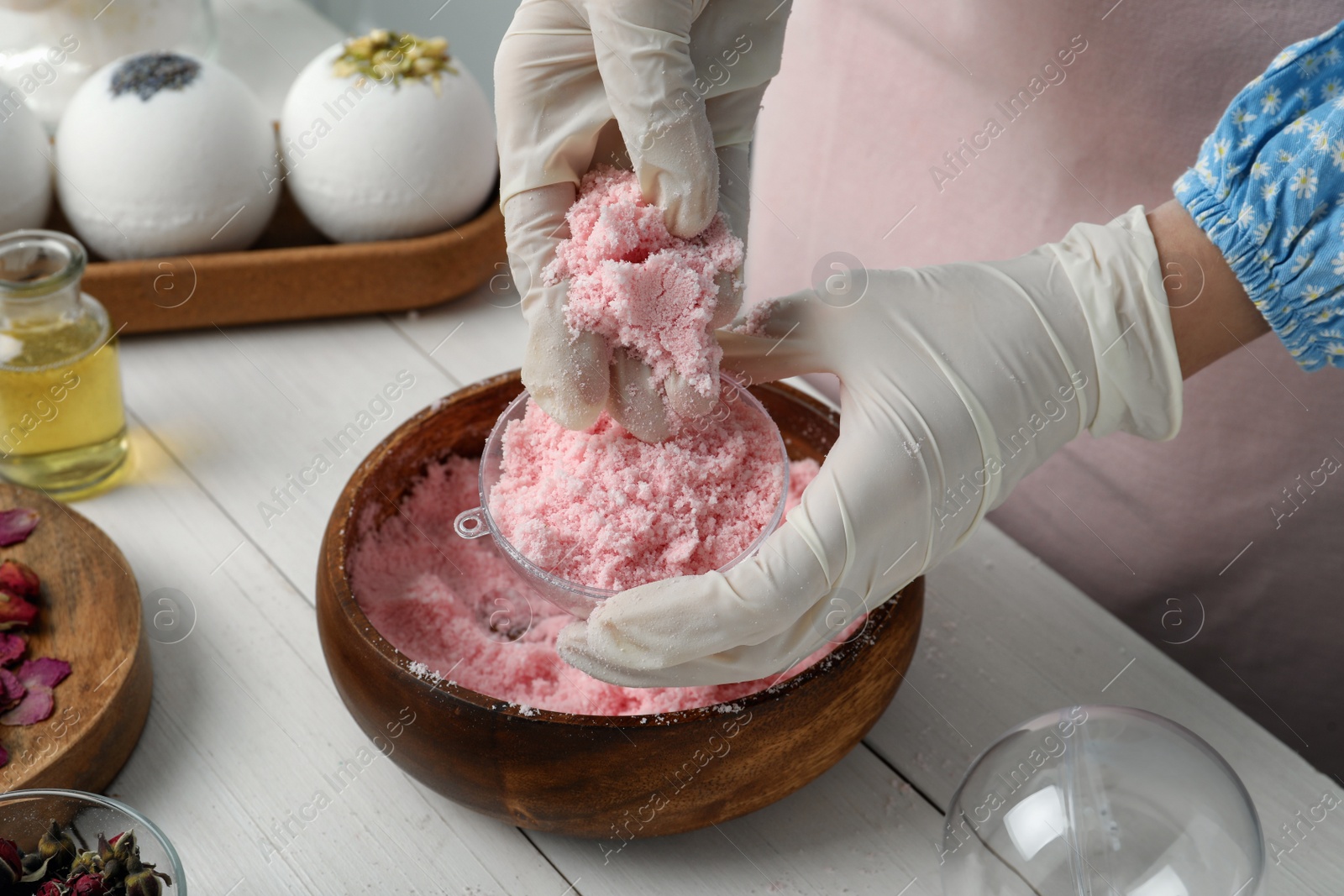 Photo of Woman in gloves making bath bomb at white table, closeup