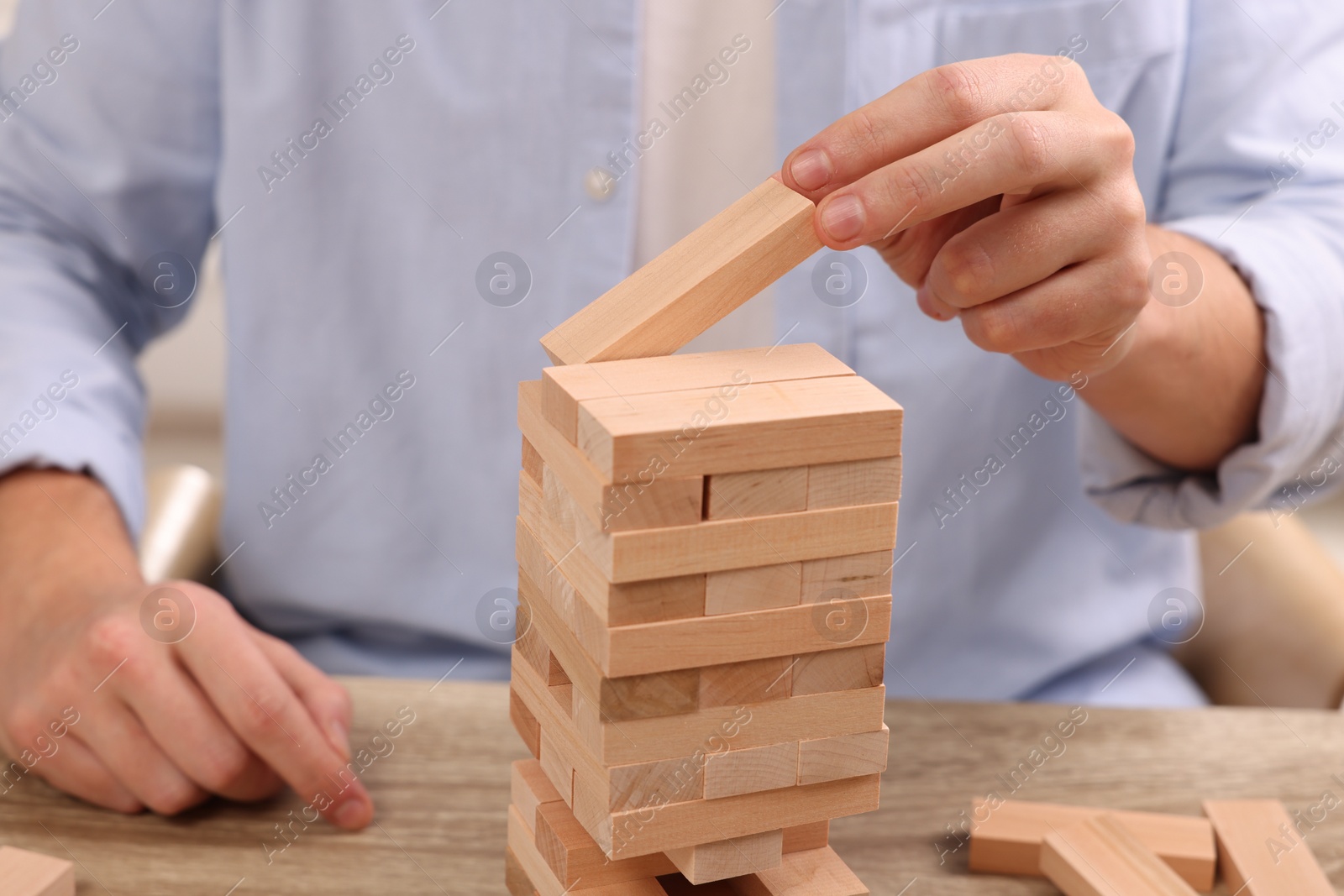 Photo of Playing Jenga. Man building tower with wooden blocks at table, closeup