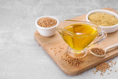 Photo of Jug of natural oil, mustard seeds and powder on light grey table. Space for text