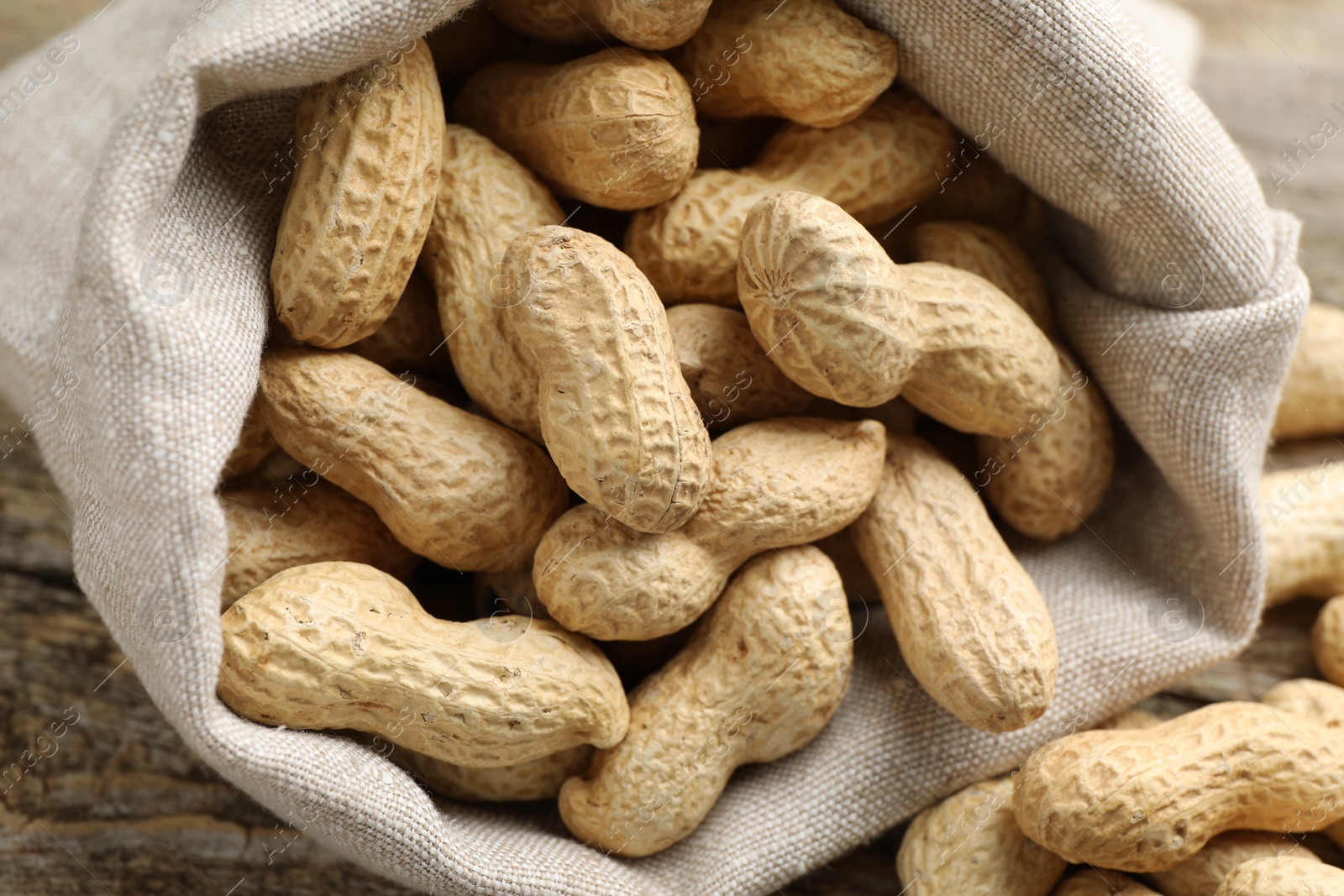 Photo of Fresh unpeeled peanuts in sack on wooden table, closeup