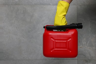 Photo of Man in rubber glove holding red canister near grey wall, closeup. Space for text