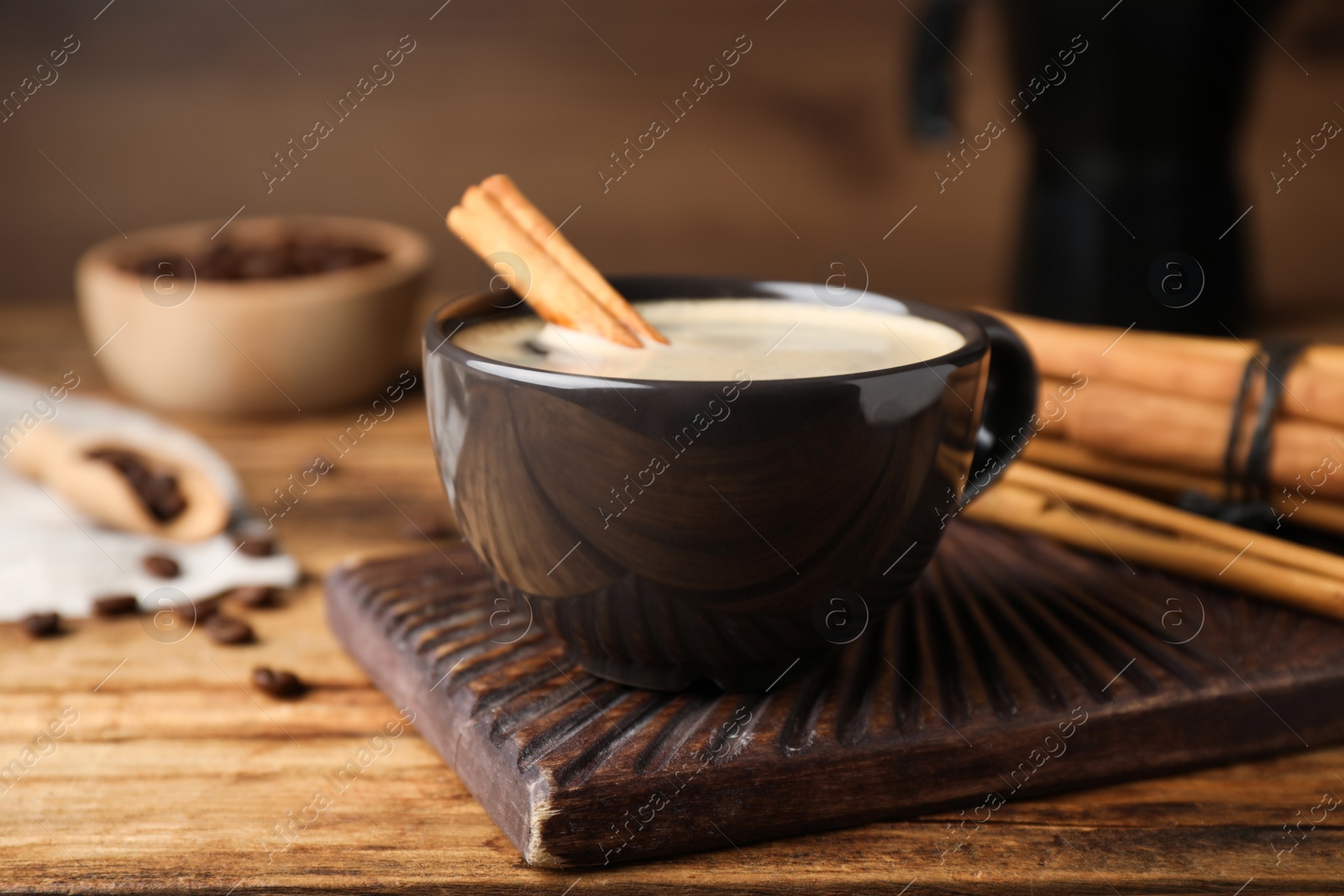 Photo of Cup of hot coffee with aromatic cinnamon on wooden table