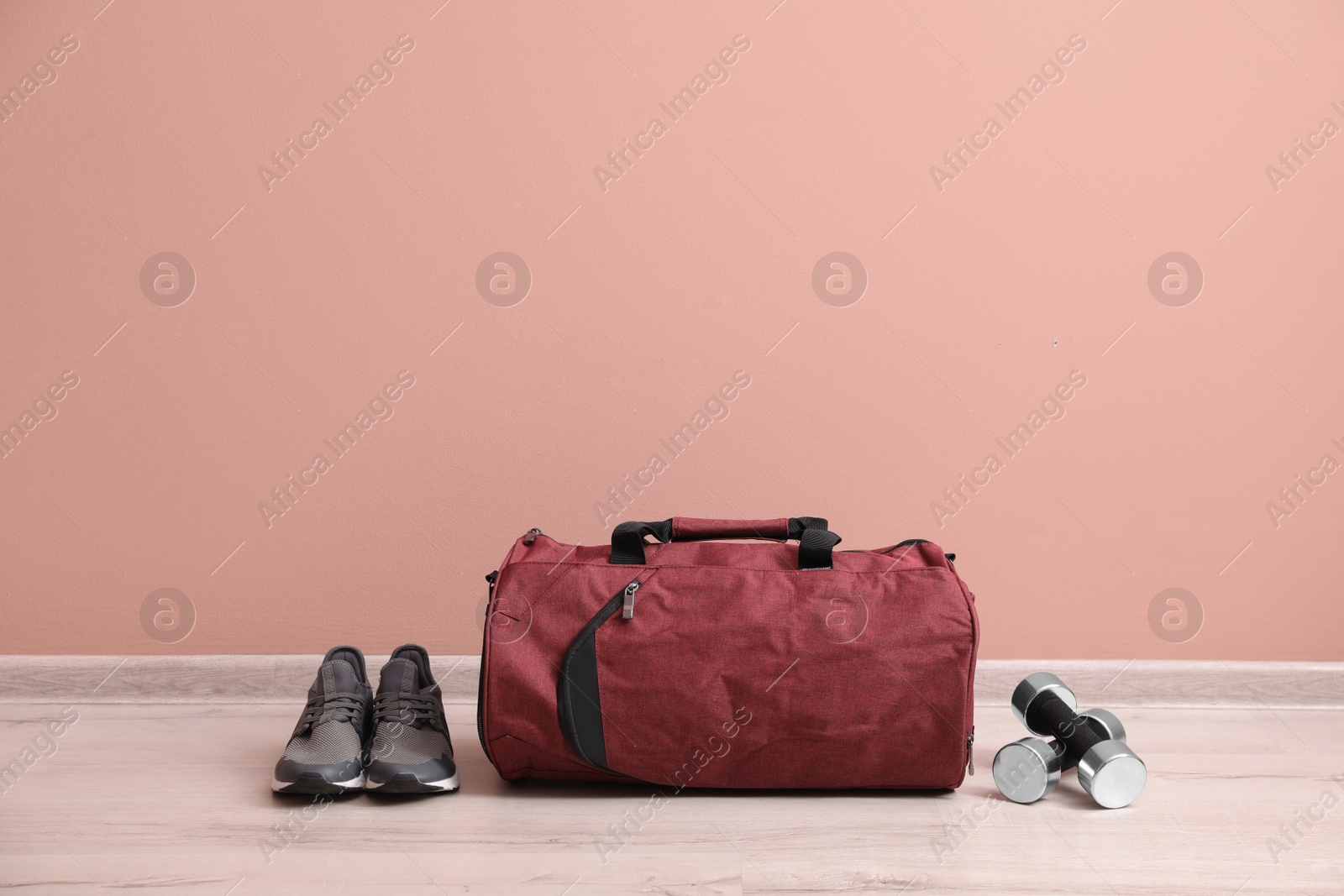 Photo of Red sports bag, sneakers and dumbbells on floor near pink wall, space for text