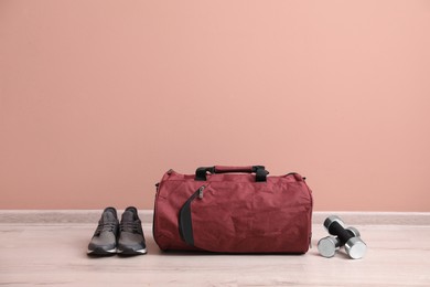 Red sports bag, sneakers and dumbbells on floor near pink wall, space for text