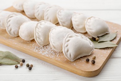 Photo of Raw dumplings (varenyky), peppercorns and bay leaves on white wooden table, closeup