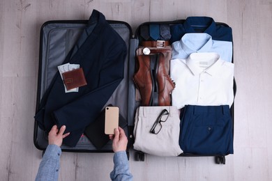 Photo of Man packing suitcase for business trip on wooden floor, top view