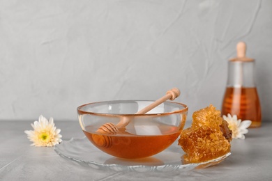 Photo of Glass bowl with tasty honey and dipper on gray table