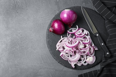 Photo of Slate plate with cut and whole red onions on grey table, top view. Space for text