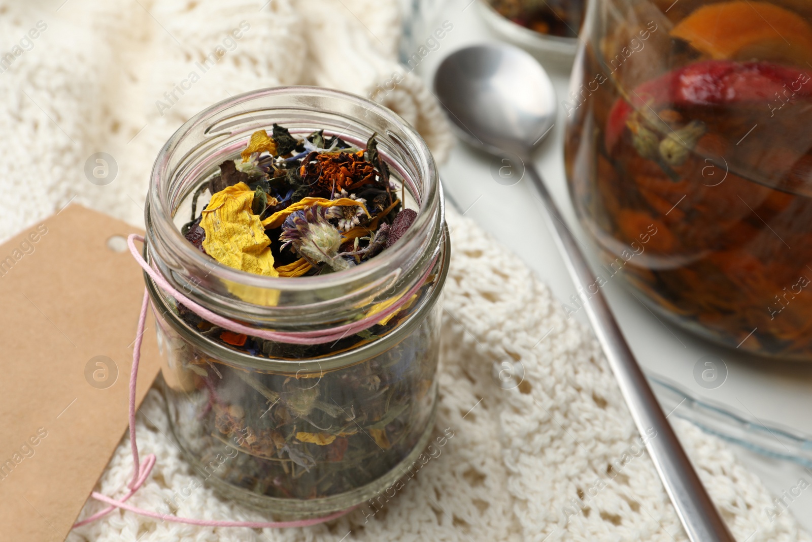 Photo of Glass jar with dry herbal tea and knitted fabric on table, closeup