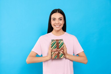 Photo of Happy young woman holding gift box on light blue background