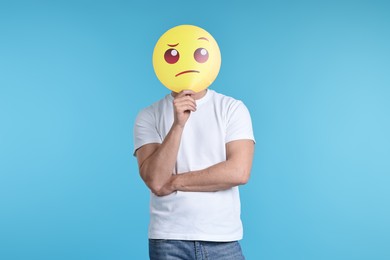 Photo of Man covering face with thinking emoticon on light blue background