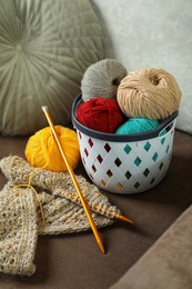 Photo of Soft woolen yarns, knitting and needles on brown sofa