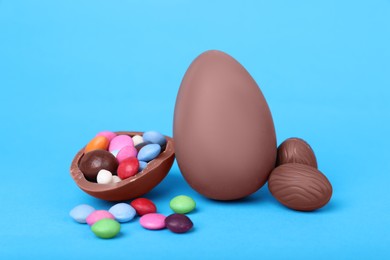 Photo of Delicious chocolate eggs and candies on light blue background, closeup