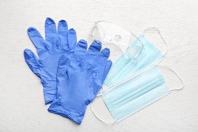 Photo of Medical gloves, masks and goggles on white wooden background, flat lay