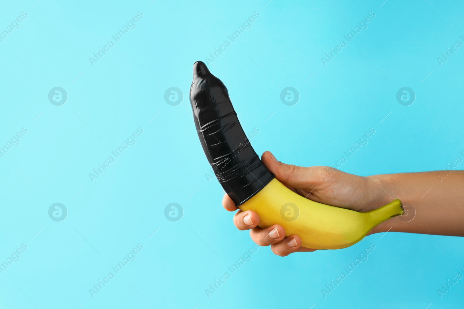 Photo of Woman holding banana in condom on light blue background, closeup and space for text. Safe sex concept