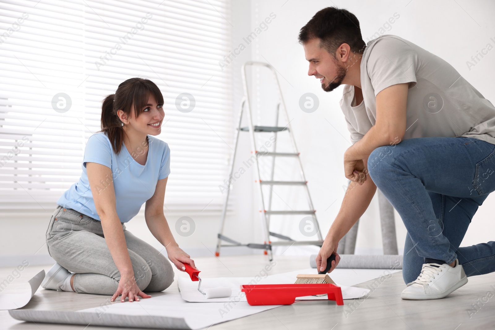 Photo of Couple applying glue onto wallpaper sheet in room