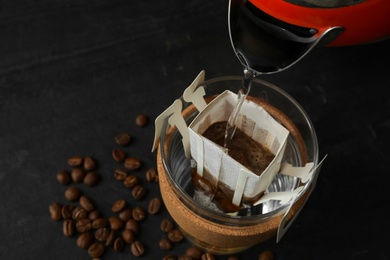 Pouring hot water into cup with drip coffee bag on black table, closeup