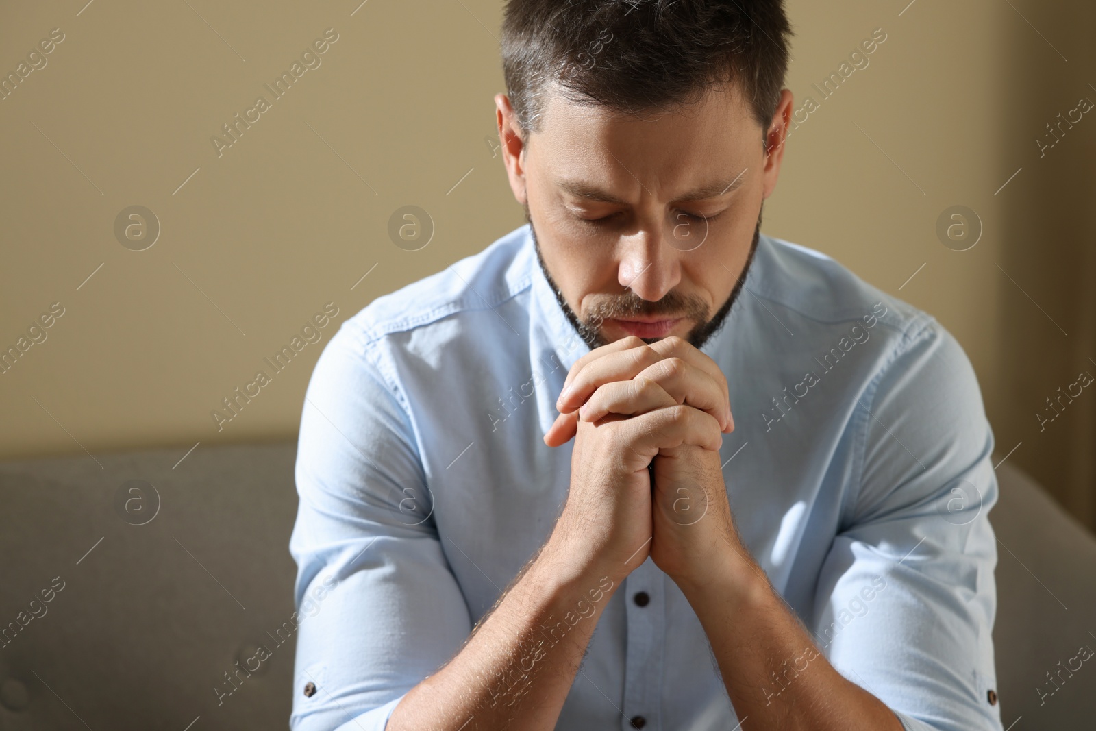 Photo of Religious man with clasped hands praying indoors