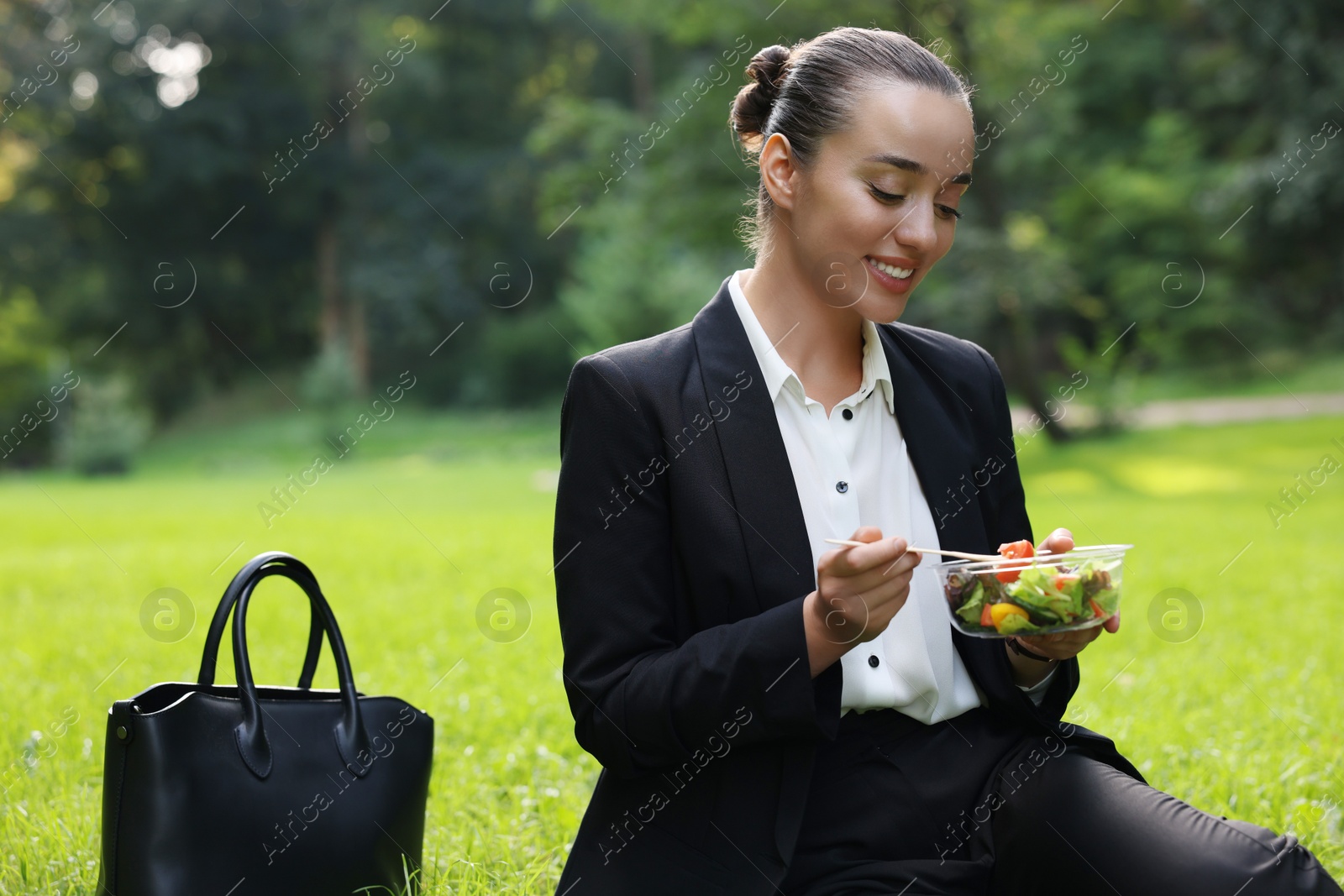 Photo of Lunch time. Happy businesswoman eating salad on green grass in park