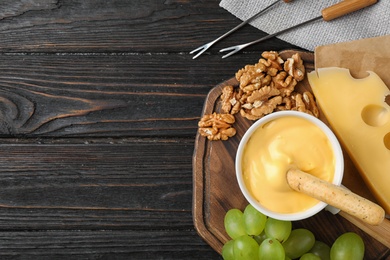 Photo of Flat lay composition with pot of tasty cheese fondue on black wooden table, space for text