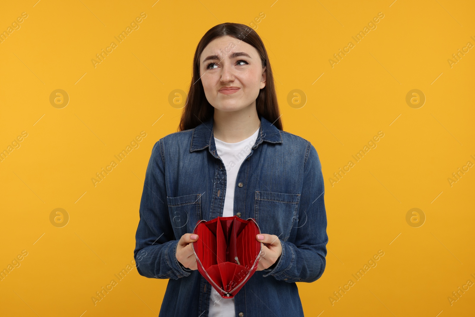 Photo of Sad woman showing empty wallet on orange background