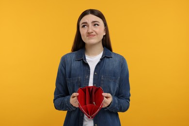 Sad woman showing empty wallet on orange background