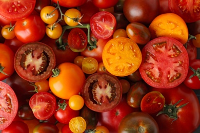 Many fresh ripe whole and cut tomatoes as background, top view