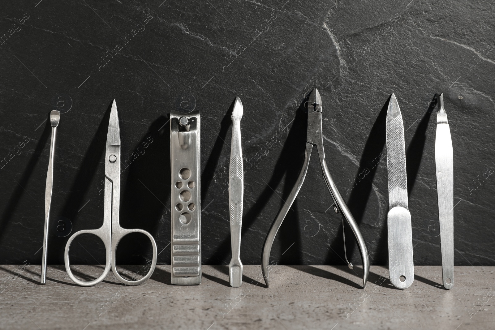 Photo of Set of manicure tools on grey table near black wall