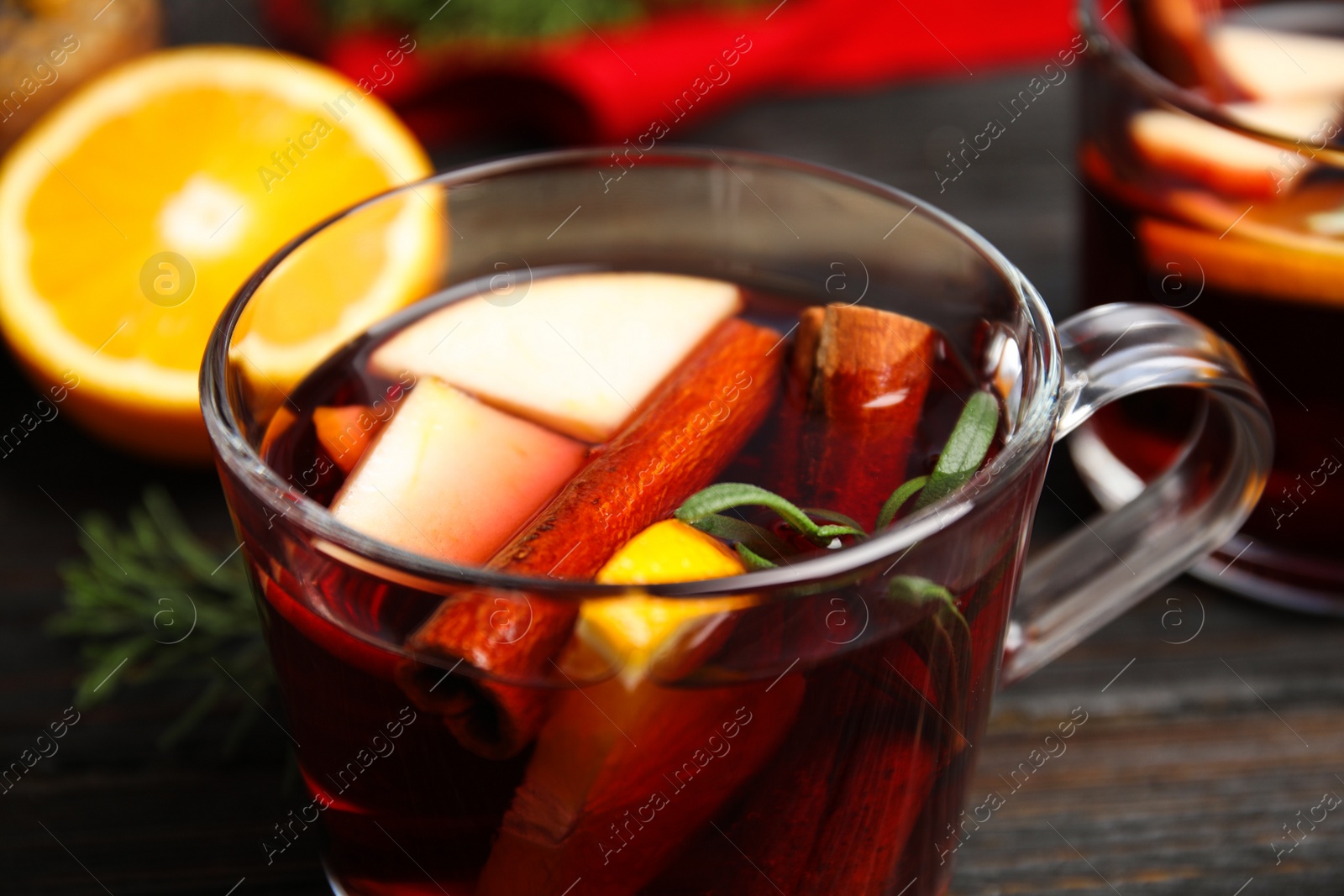 Photo of Tasty mulled wine with spices in glass cup on wooden table, closeup