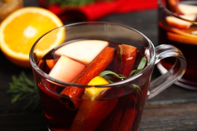 Photo of Tasty mulled wine with spices in glass cup on wooden table, closeup