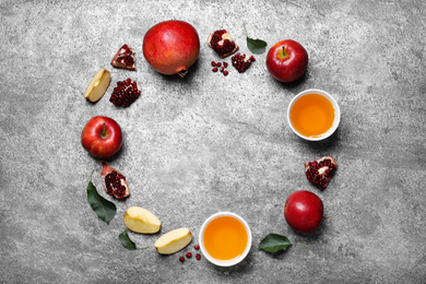 Photo of Frame of honey, apples and pomegranates on grey table, flat lay with space for text. Rosh Hashanah holiday
