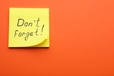Photo of Paper note with phrase Don t Forget on orange background, top view. Space for text