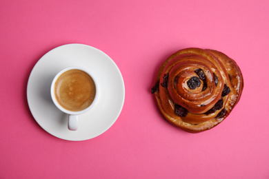 Delicious coffee and bun on pink background, top view. Sweet pastries