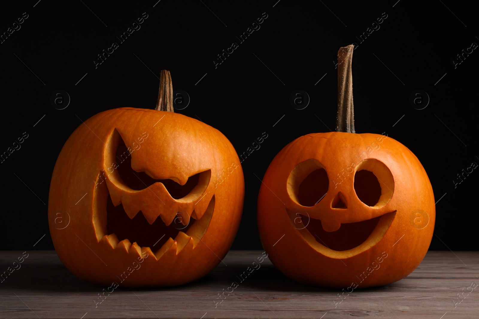 Photo of Scary jack o'lanterns made of pumpkins on wooden table against black background. Halloween traditional decor