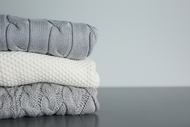 Stack of folded knitted sweaters on grey table. Space for text