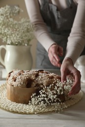 Photo of Woman decorating delicious Italian Easter dove cake (traditional Colomba di Pasqua) with flowers at white wooden table, closeup