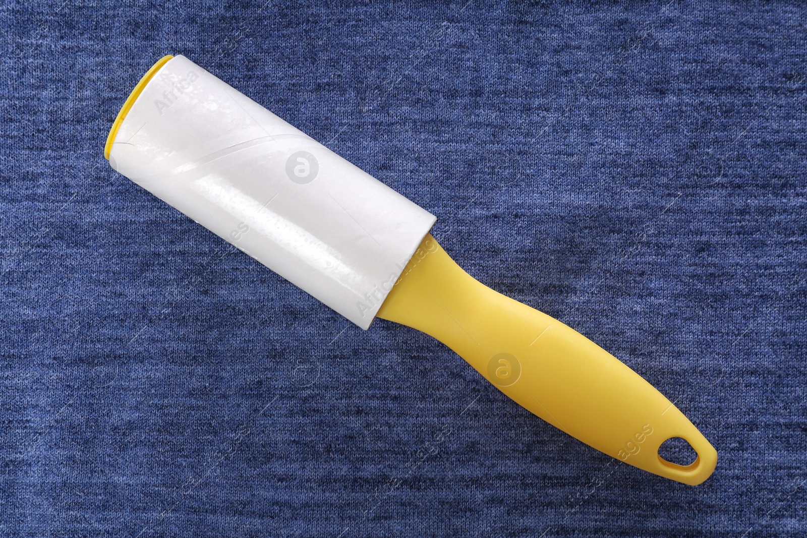 Photo of New lint roller with yellow handle on blue fabric, top view