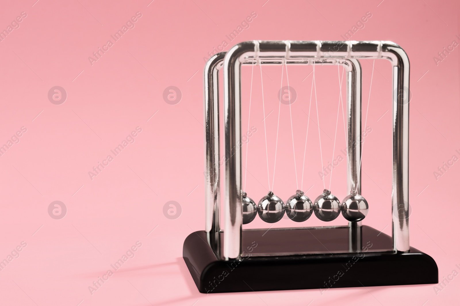 Photo of Newton's cradle on pink background, space for text. Physics law of energy conservation