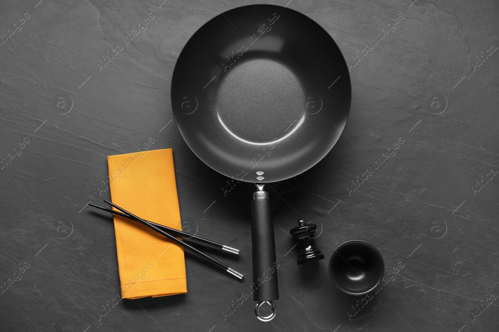 Photo of Empty iron wok, sauce bowl and chopsticks on black table, flat lay