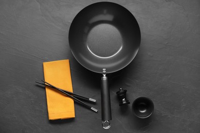 Photo of Empty iron wok, sauce bowl and chopsticks on black table, flat lay