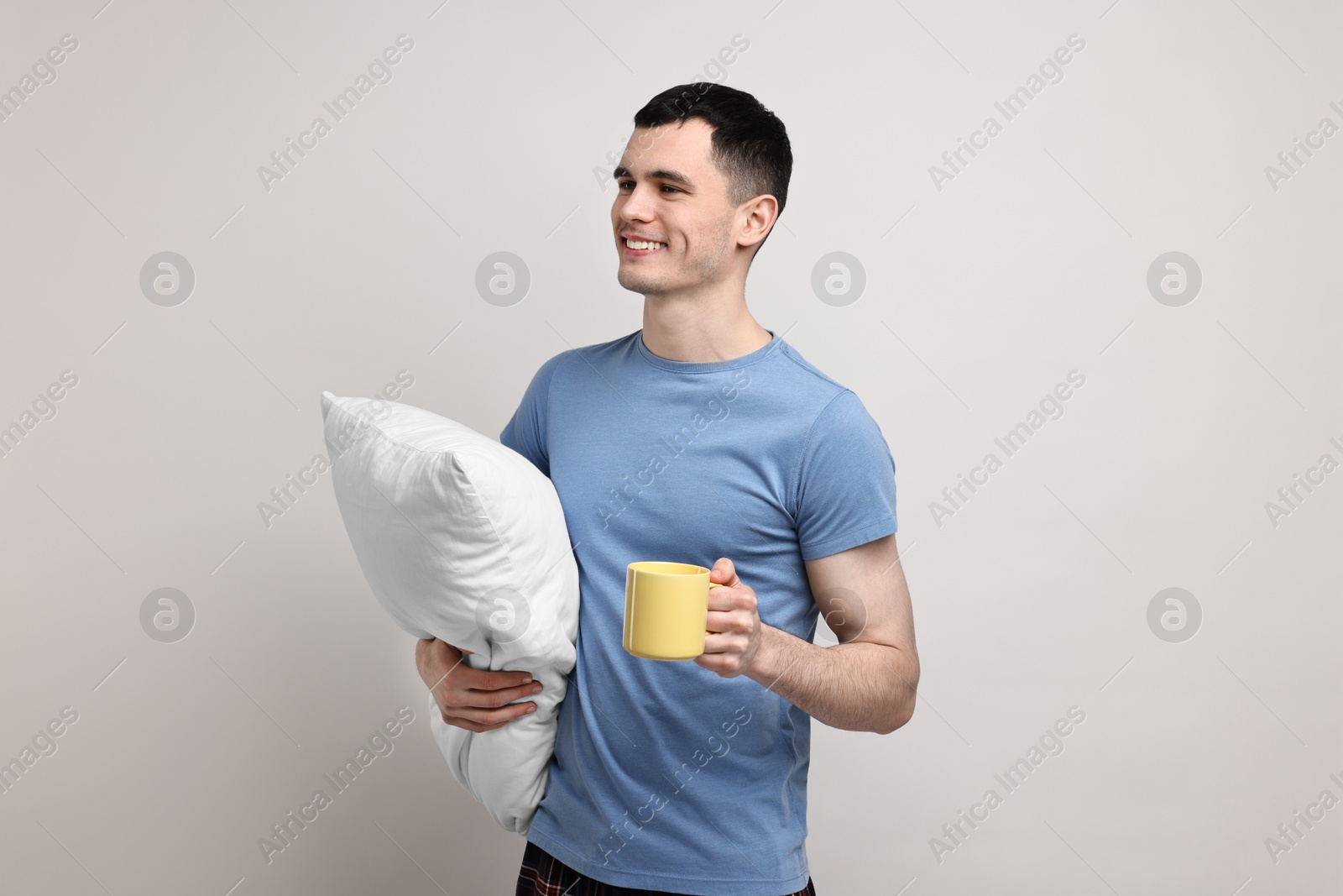 Photo of Happy man in pyjama holding pillow and cup of drink on light grey background
