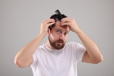 Dandruff problem. Man with comb examining his hair and scalp on light gray background