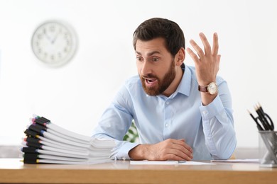 Emotional businessman with documents at wooden table in office