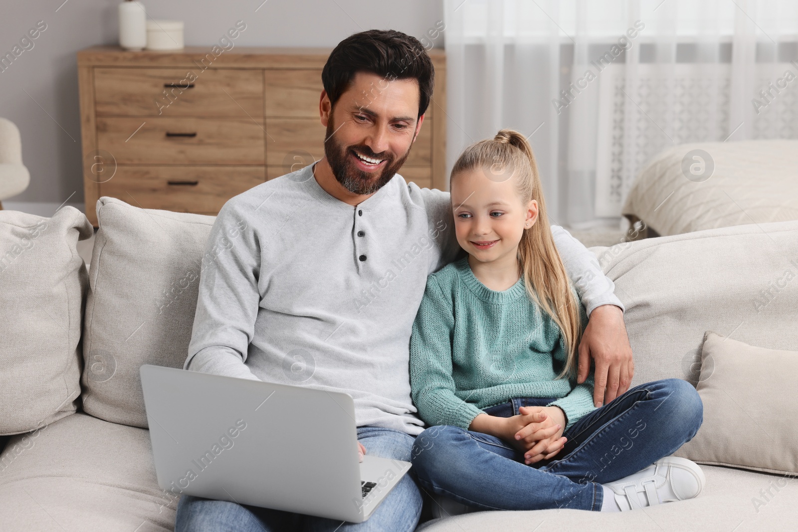 Photo of Happy man and his daughter with laptop on sofa at home