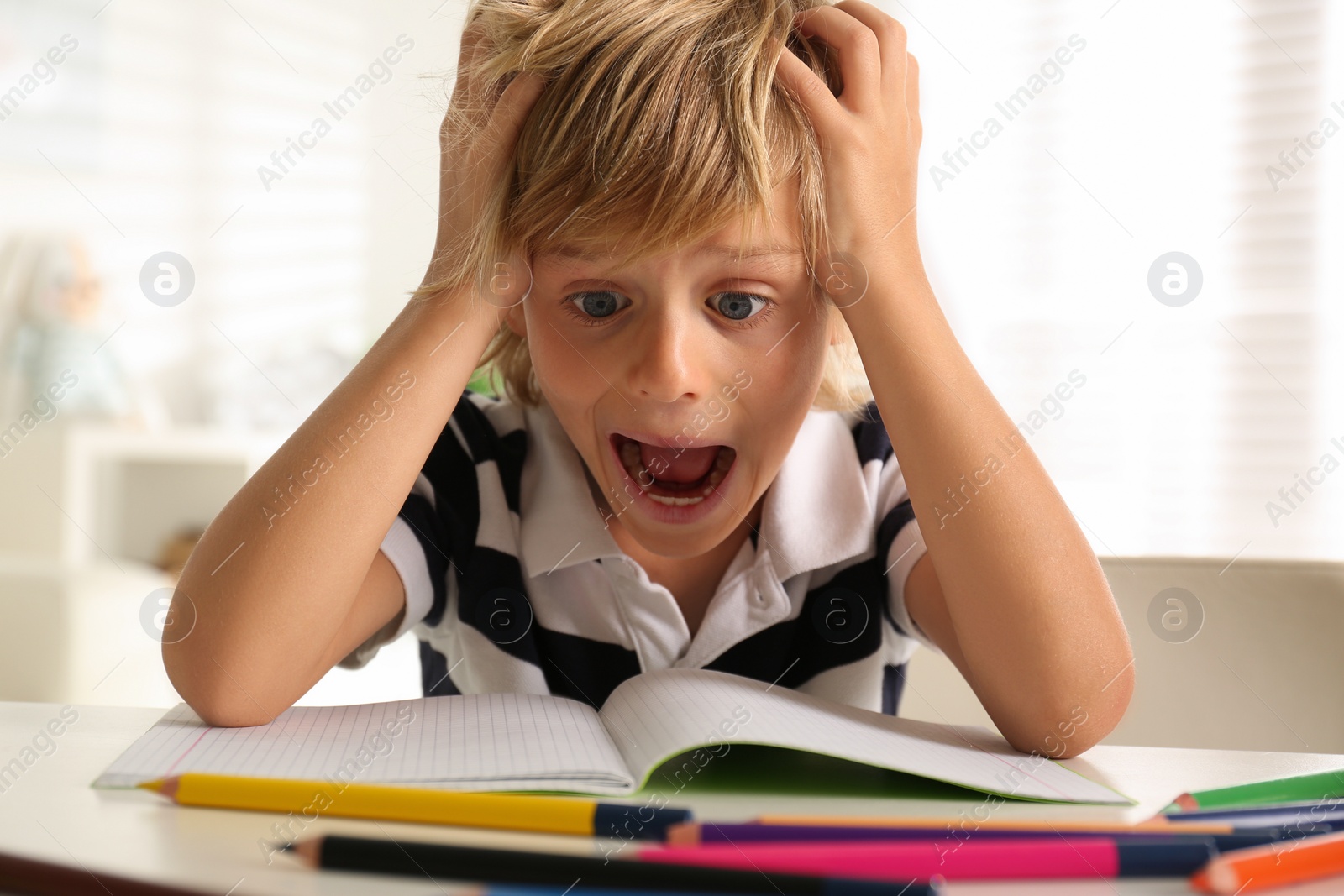 Photo of Emotional little boy doing homework at table indoors