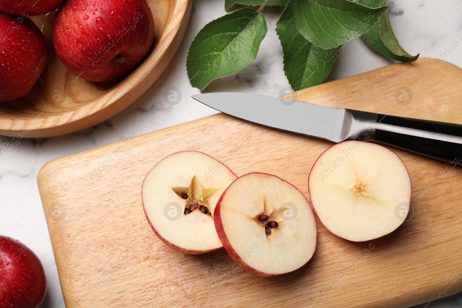 Photo of Cut red apple, knife and green leaves on white marble table, above view