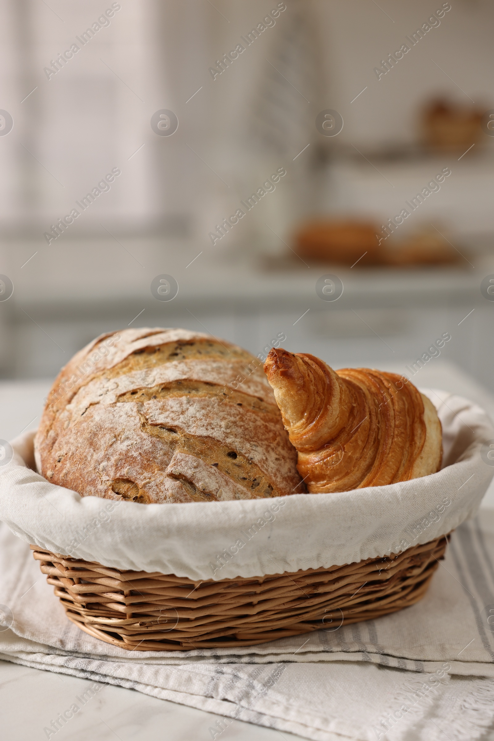 Photo of Wicker bread basket with freshly baked loaf and croissant on white marble table in kitchen