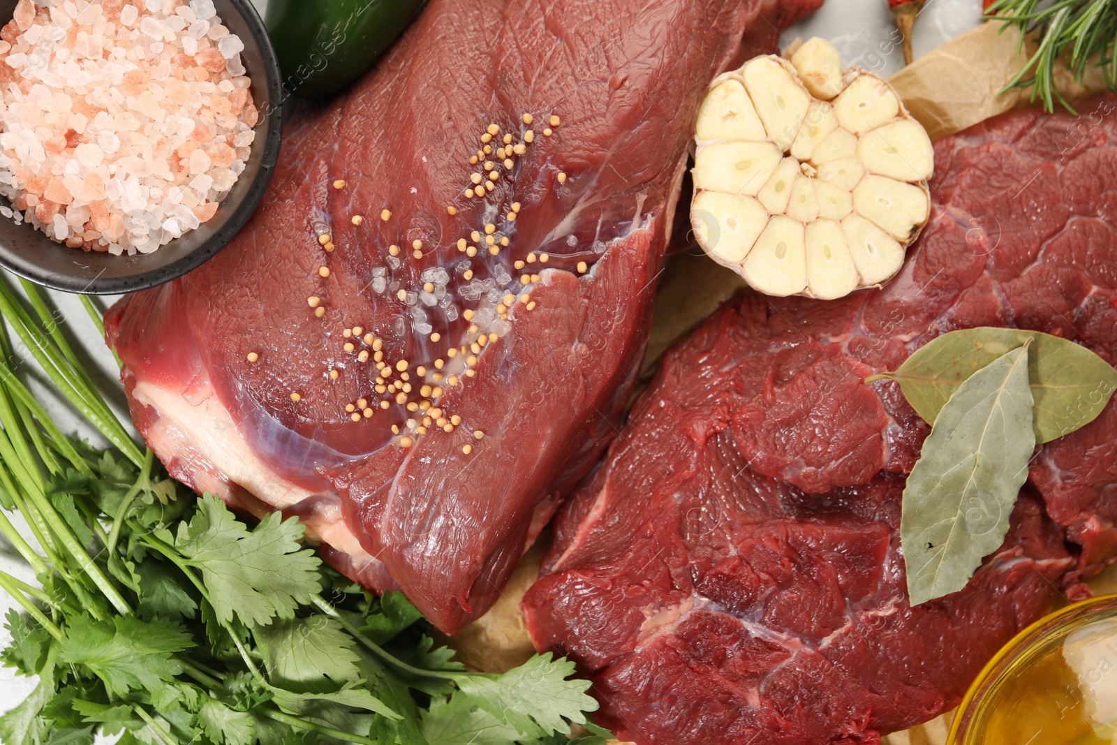 Photo of Pieces of raw beef meat, parsley and spices on table, flat lay